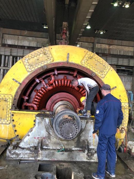 Generator stator opened for overhaul with technicians working inside the machine hall